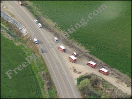 Aerial view showing fields and dusty roads; also some red-and-white trucks and other white coloured vehicles