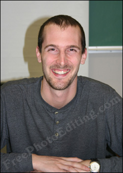Photo to be edited to remove background, so that focus is on man. This an agreeable young man smiling. Wearing grey full-sleeved sweat shirt. Hands are in front, one over the other. Round-dialled watch is visible on left wrist. 