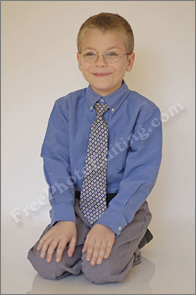 Before photo editing: Photo of calm looking, bespectacled 10-year-old boy in blue shirt, grey trousers and tie, kneeling down, hands on knees. Photo has a plain background.