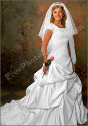 Before photo editing: Photo of a bride in flowing white bridal gown, holding a rose, shot against a studio backdrop. The bride needs a background change; she is to be transposed to a nature setting. 