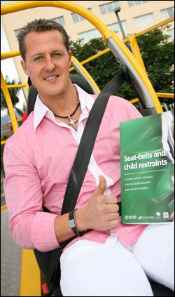 Photograph of Michael Schumacher with FIA Foundation's 'Seat-belts and Child Restraints' manual. The Formula 1 champ is wearing a pink shirt and a 'cross' around his neck.