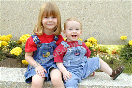 Photo of two little children -- brother and sister -- sitting in front of a marigold bed.